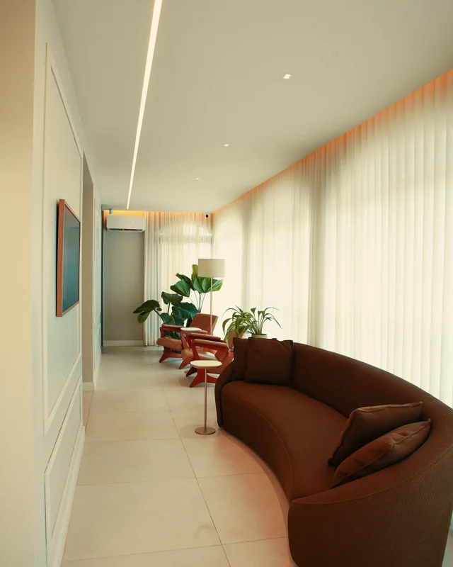 Sala de espera da Clínica Maví, com sofá curvo, poltronas de madeira, plantas e luz natural